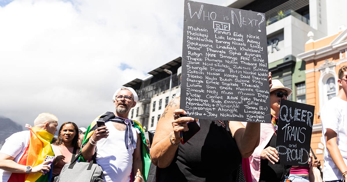 A photo of an individual holding up a placard with the many names of murdered members of the LGBT+ community.